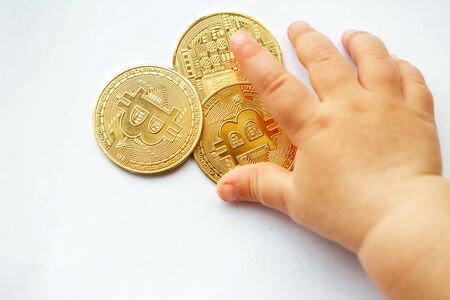 The baby chooses bitcoin, he plays with coins. Close-up, white backgroundの写真素材