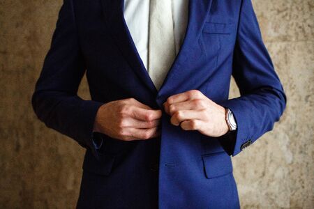 a man fastens buttons blue jacket on his hand his watch. No face, close-upの写真素材