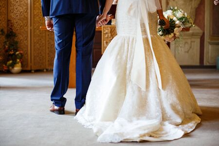 The bride and groom hold hands in front of the altar. view from the backの写真素材