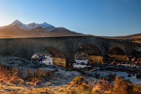 old stone bridge near the town of Sligachan overlooking the snowy mountainsの写真素材