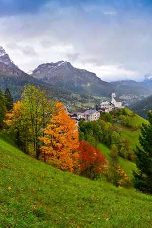 autumn landscape with colorful trees and snowy mountains in the background in Dolomites, the village of Colle Santa Lucia as seen from Passo Giauの写真素材