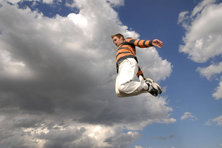 Young man happily jumping against blue sky.