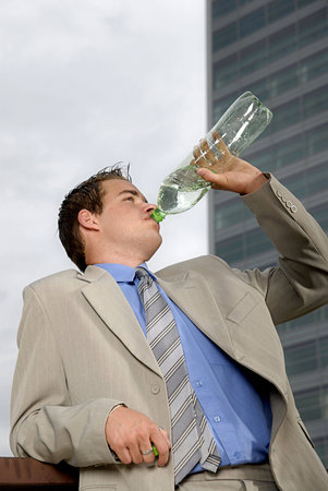Businessman drinking water from plastic bottle in front of business building.