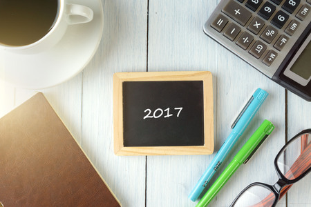 top view of 2017 written on the chalkboard,business concept.chalkboard,notebook,calculator,pen,glasses,coffee on the wooden desk.の写真素材
