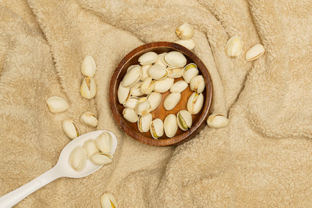 Flat lay of healthy grains concept, Pistachios in wooden bowl and spoon on wool blanket.の写真素材
