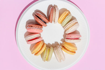 French dessert concept, Circle arrangement of colorful macarons in white plate on pink background.の写真素材