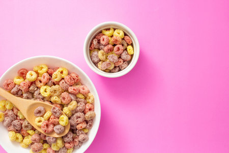 Healthy food concept, Colorful ring cereals in bowl with spoon and mini bowl on pink background.