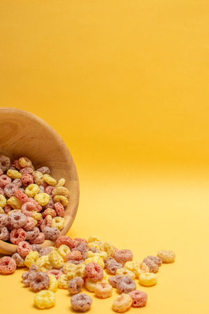Breakfast cereal concept, Colorful ring cereals is poured out of a wooden bowl on yellow background.