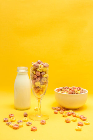 Healthy breakfast concept, Colorful ring cereals in glass and bowl with milk on yellow background.
