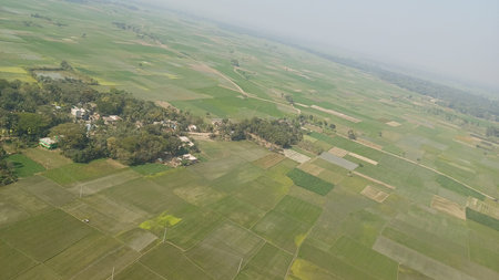 an aerial view of a small village surrounded by green fields and trees on a hazy day