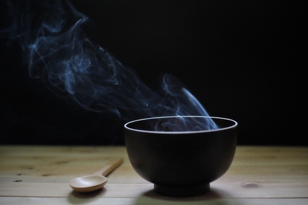 Hot soup in bowl with smoke on wood table and black backgroundの写真素材