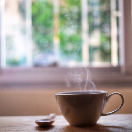a cup of hot coffee steam smoke on wood table with window background.の写真素材