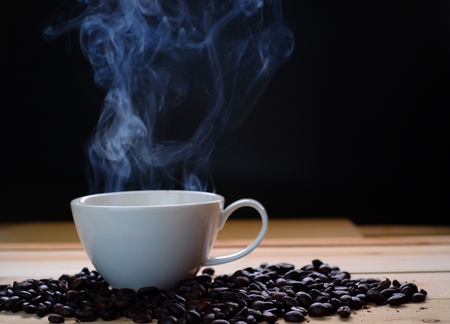 Coffee cup and coffee beans on wooden table with hot smoke, black background.の写真素材