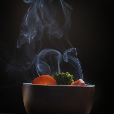 Bowl of hot food with steam smoke on wood table and black background soft focusの写真素材