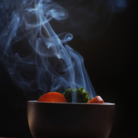 Bowl of hot food with steam smoke on wood table and black background soft focusの写真素材