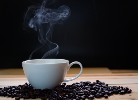 Coffee cup and coffee beans on wooden table with hot smoke, black background.の写真素材
