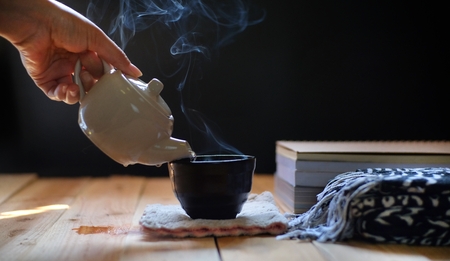Pouring hot tea in teapot and cup on wood table, black background. Winter tea time.の写真素材