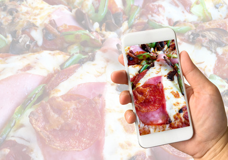 Woman hand holding smartphone against pizza background food online conceptの写真素材