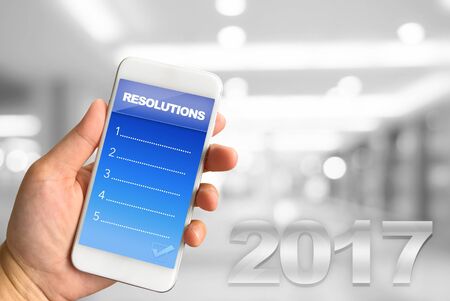 Woman hand holding smartphone against white grey bokeh abstract background Resolutions conceptの写真素材