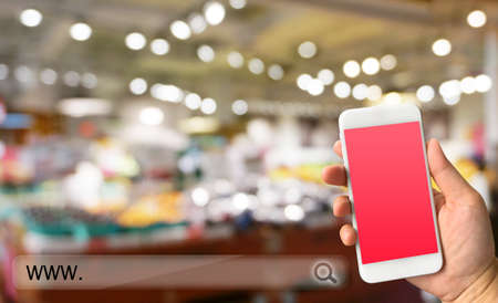 Woman hand holding smartphone against blur bokeh ofstore background online shopping conceptの写真素材