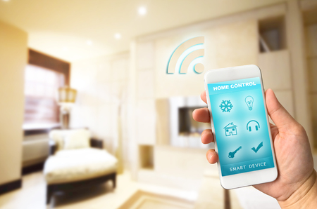 Woman hand holding smartphone against blur of living room background smart home control conceptの写真素材