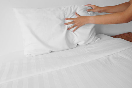 woman hands set up white pillow on bed sheet in hotel room