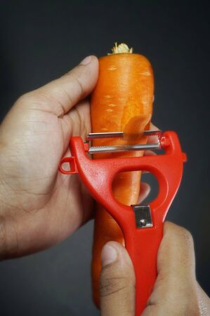 Raw peeled carrot with red peeler isloated on black/dark background.の写真素材