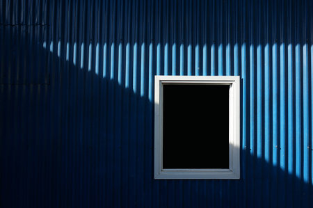 white window on blue metal wall with sunlight and shadow.の写真素材