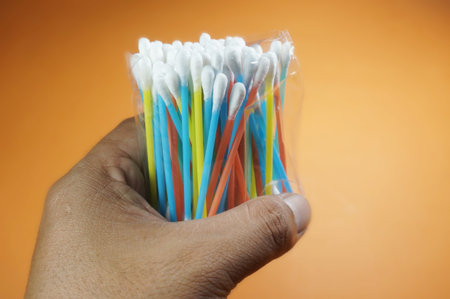 Hand holding colorful cotton bud, Isolated on orange background.