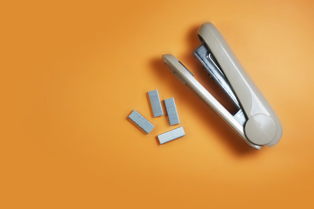 Big stapler and small staples isolated on orange background.