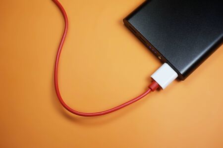 powerbank charges with red cable isolated on orange backgroundの写真素材
