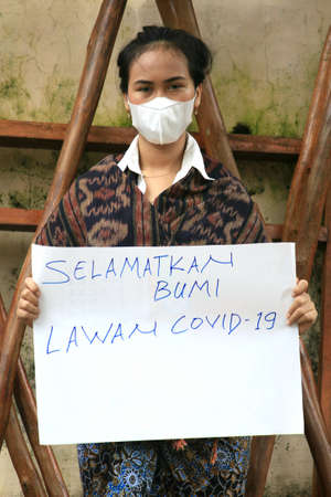 Pekalongan, Indonesia - 1 February 2021: a girl holds a banner that says "Selamatkan Bumi Lawan Covid-19" (Save The Earth Fight Covid-19)のeditorial素材