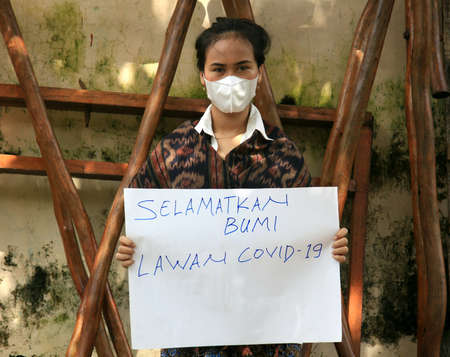 Pekalongan, Indonesia - 1 February 2021: a girl holds a banner that says "Selamatkan Bumi Lawan Covid-19" (Save The Earth Fight Covid-19)のeditorial素材