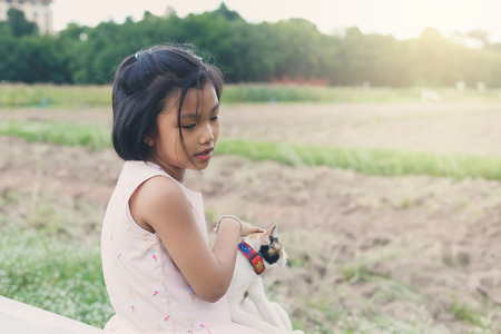A cute girl sitting and her playing a cat on planting plotの写真素材
