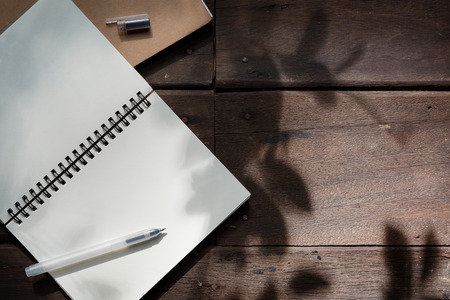 Pen and recycle notebook on wood background with shadow of Leavesの写真素材