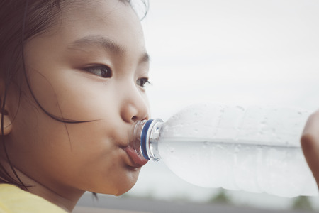Cute girl is drinking water from plastic bottle. Clean water will help solve the thirst for her.の写真素材