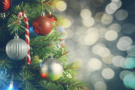 A shiny silver Christmas ornament hangs on a Christmas tree, next to a bright candy cane. This festive scene is perfect for holiday cards, social media promotions, or seasonal design projects.の素材