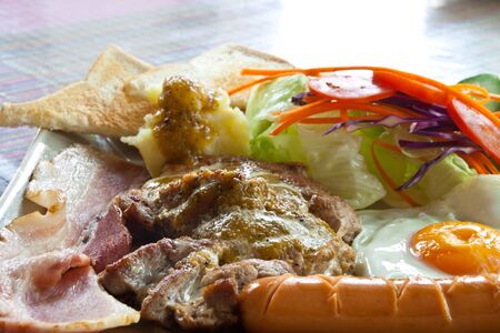 Steak pork, bacon, fried egg, sausage, bread and salad.の写真素材