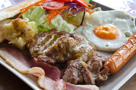 Steak pork, bacon, fried egg, sausage, bread and salad の写真素材
