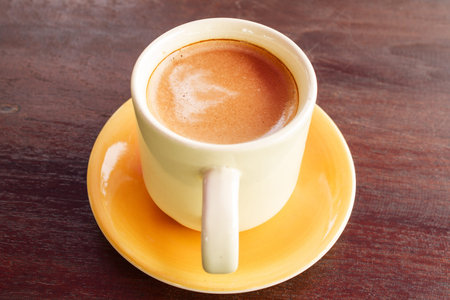 Hot coffee latte in yellow glass on a wooden brown の写真素材