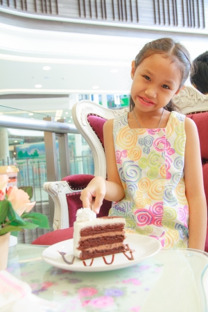 Girl eating chocolate cake sitting on a chair.の写真素材