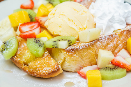 Honey toast with ice cream vanilla, kiwi, mango, banana, apple and strawberry on white plate.の写真素材