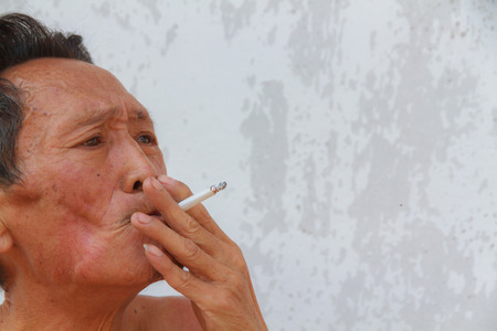 Asian old man smoking cigarette. Face filled with wrinkles.の写真素材