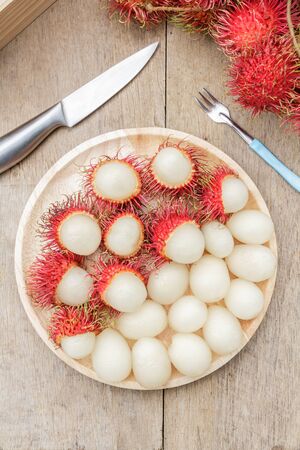 Rambutan in wooden dish and knife on wood table. Top view.の写真素材