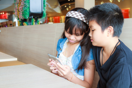 Asian boy and girl use smartphone in canteen.の写真素材