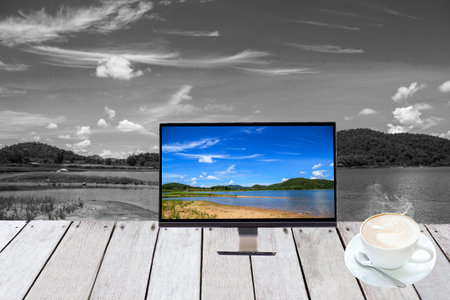 Monitor on plank wooden front show lake and hot coffee.