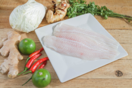 Dolly fish preparing for steaming fish with lime, chili, lettuce, ginger, galangal and parsley on wood table.の写真素材
