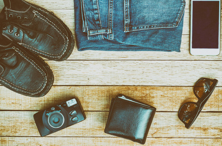 Travel casual outfits with camera, smartphone, shoes, sunglasses, wallet and jean on wooden table. travel concept vintage style, top view.の写真素材