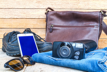 Travel casual outfits with camera, smartphone, shoes, wallet, leather bag, sunglasses and jean on wooden table. travel concept.の写真素材