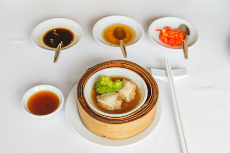 Dim sum food Steamed sliced abalone in brown sauce with broccoli in bamboo basket at restaurant with soy sauce, sweet sauce, chili sauce and chopsticks.の写真素材